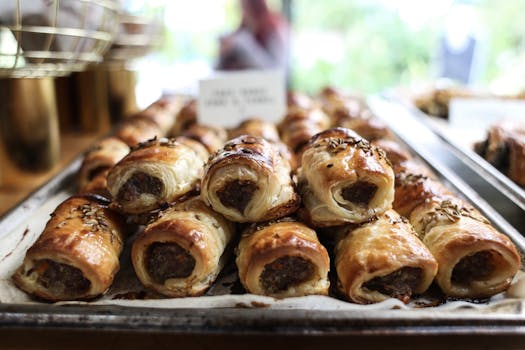 Close-up of freshly baked sausage rolls with flaky pastry and seasoning on a tray.
