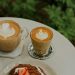 Enjoy a delightful outdoor brunch featuring cappuccinos with latte art and a strawberry pastry.