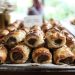 Close-up of freshly baked sausage rolls with flaky pastry and seasoning on a tray.