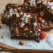Delicious brownies adorned with nuts, raspberries, and flowers on a wooden table.
